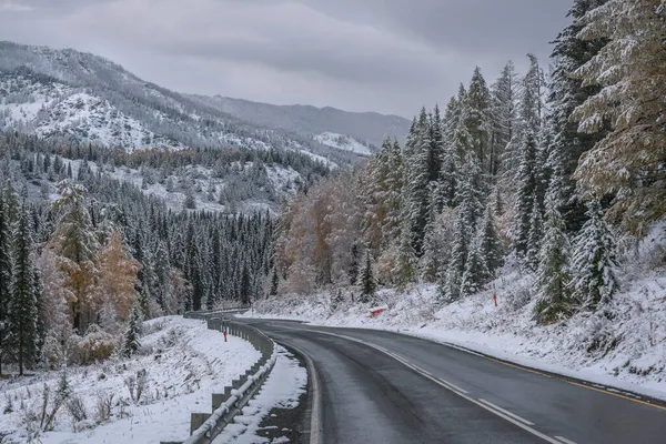 山の中のぬれた曲がりくねったアスファルトの道路と絵のような秋の風景 峠からの降下 道路脇の雪と森 曇りの日の斜面 — ストック写真