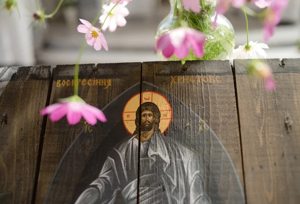 Wooden icon of the Resurrection of Jesus Christ surrounded by pink wildflowers