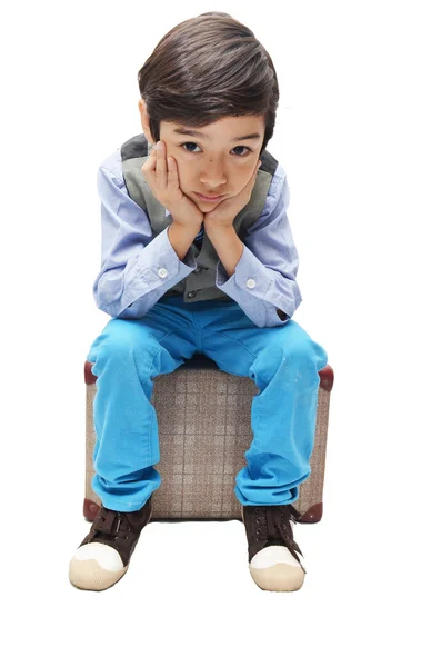 Menino sentado na bagagem com rosto triste no fundo branco — Fotografia de Stock
