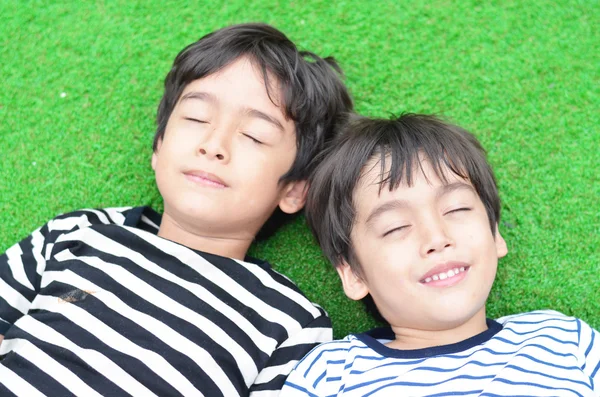 Kleiner Geschwisterjunge legt die Augen eng ins Gras — Stockfoto