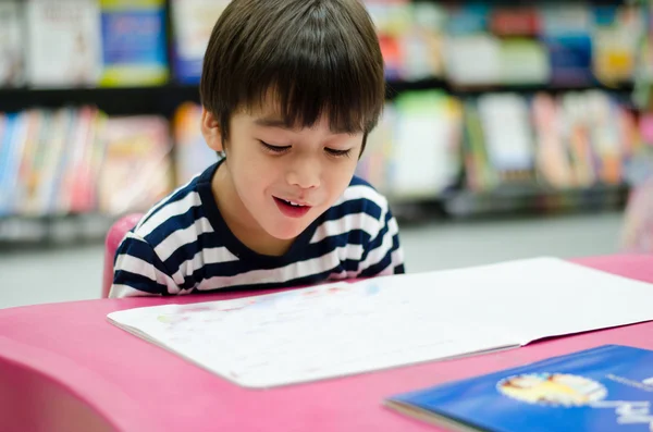 Liten pojke i biblioteket läser bok — Stockfoto