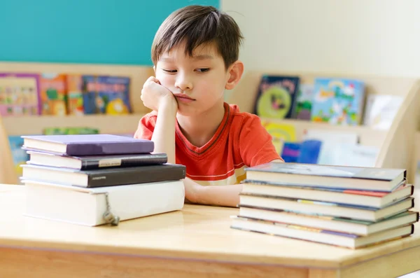 Liten pojke läsa boken på bordet hemma med tråkig ansikte — Stockfoto