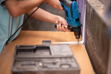 Genç oğlan tornavida kullanıyor, tahta masayı tamir ediyor.