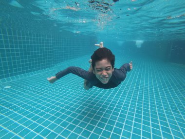 Küçük çocuk havuzun altında mutlu bir gülümseme ile eğleniyor.