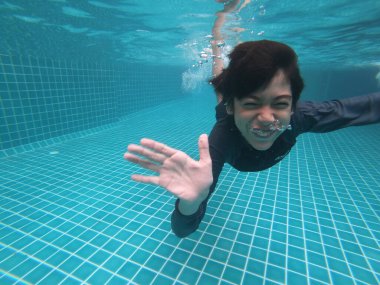 Küçük çocuk havuzun altında mutlu bir gülümseme ile eğleniyor.