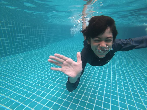 Küçük çocuk havuzun altında mutlu bir gülümseme ile eğleniyor.