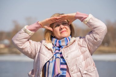 Nehrin kıyısında duruyor. Boynunda bir ceket ve atkı var. Güneş ışığından korunuyor. Bakış mesafeye ve geleceğe yönelir. Arkaplan kıyısı rezervuarına karşı.