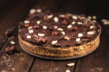 Fıstıklı yuvarlak çikolatalı pasta ve ahşap arka planda fındık.