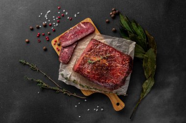 Ahşap kesme tahtasının üzerinde kırmızı tütsülenmiş jambon parçasıyla yaşam kompozisyonu.