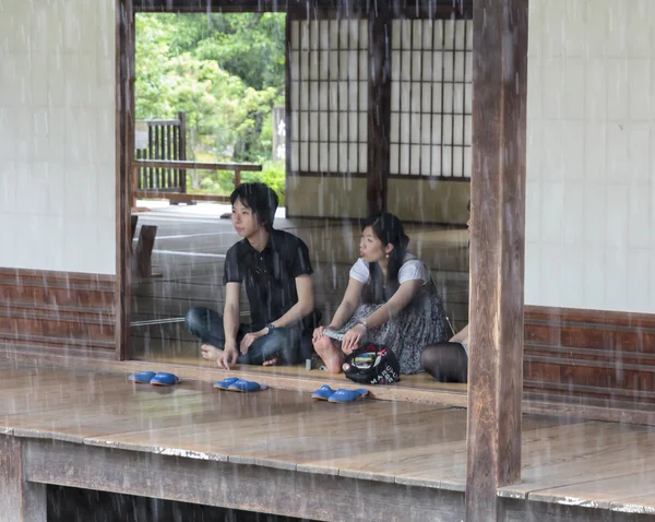 A young Japanese couple look at the rain from the temple buildi — Stock Photo, Image
