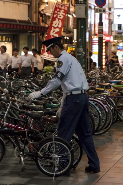 Um guarda ajusta bicicletas estacionadas na rua em Osaka, Japão — Fotografia de Stock