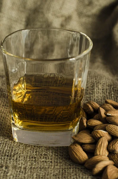 Glass of scotch whiskey on wool sack with almond seeds — Stock Photo, Image