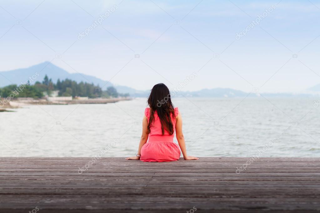 Sad woman sitting alone on a jetty.