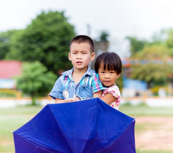 Un niño sonriente y una niña pequeña con paraguas en el parque — Foto de Stock