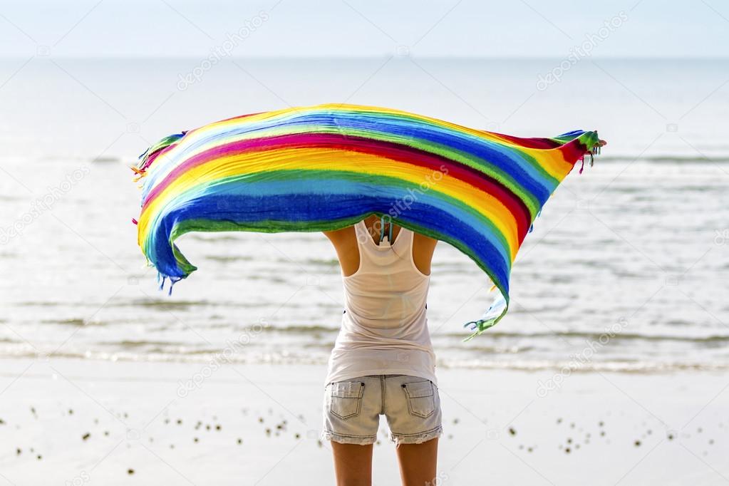 Girl in the beach holding a colored piece of fabric