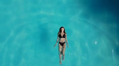 Havuz manzarasında, sırtüstü yüzen mayo giymiş güzel bir kız. Bir İHA 'dan alındı.