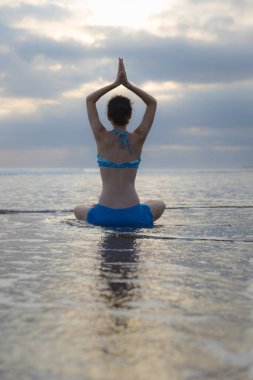 Bali 'de günbatımı plaj yoga antrenmanı. Lotus pozu. Padmasana. Eller namaste mudra 'da. Meditasyon ve konsantrasyon. Zen hayatı. Bedensel ve zihinsel rahatlama. Yoga inzivası. Arkadan bak. Boşluğu kopyala.