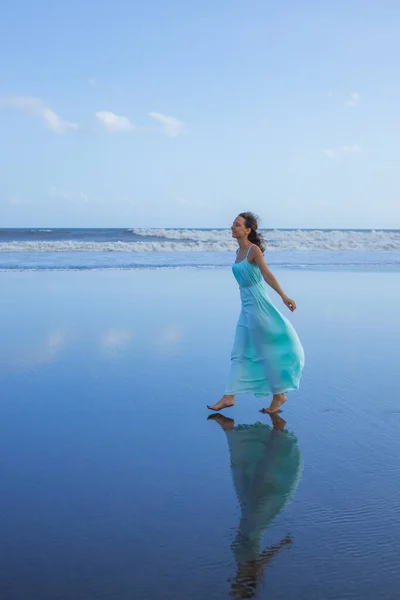 笑顔の女性が空のビーチで裸足で歩く 全身肖像画 スリム白人女性は長いドレスを着ている 水の反射 幸せと自由 アジアでの夏休み 旅行のコンセプト バリ島 — ストック写真
