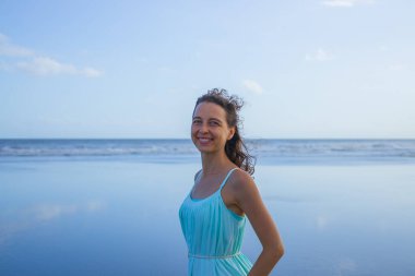 Kumsaldaki güzel beyaz kadın portresi. Asya 'da yaz tatili. Elbise giymiş gülümseyen genç bir kadın. Güneşli bir gün. Mavi gökyüzü. Ufuk çizgisi olan okyanus. Seyahat yaşam tarzı. Bali, Endonezya.