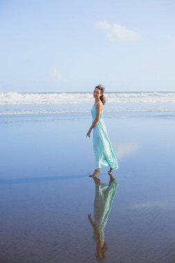 Genç bir kadın boş sahilde yalınayak yürüyor. Tam vücut portresi. İnce beyaz kadın, uzun elbise giyiyor. Sahilde iyi eğlenceler. Asya 'da yaz tatili. Seyahat konsepti. Bali, Endonezya