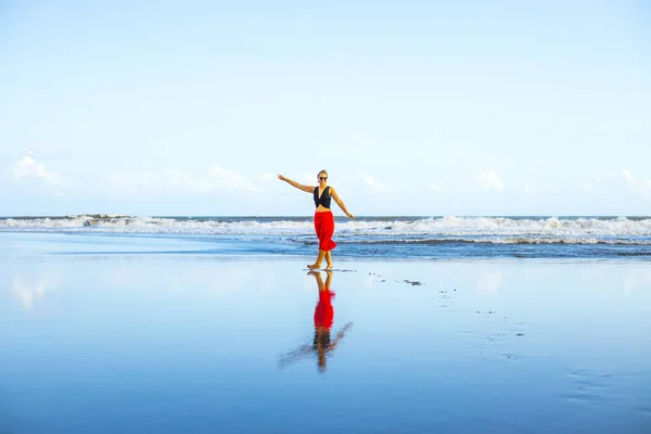 幸せな女性は裸足でビーチを歩く 全身肖像画 赤いスカートを着た白人女性 ビーチで時間をお楽しみください 水の反射 アジアでの夏休み 旅行のコンセプト インドネシアのバリ — ストック写真