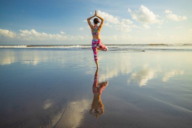 Açık hava yoga. Vrikshasana asana. Sıska kadın sahilde ağaç pozisyonu yapıyor. Su yansıması. Mükemmel denge. Yoga inzivası. Arkadan bak. Namaste Mudra 'da eller havaya. Uzayı kopyala Bali