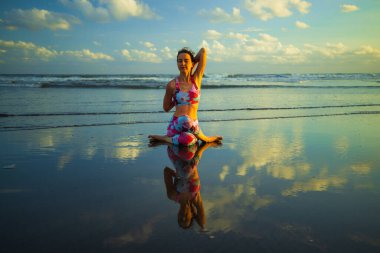 Beach yoga. Attractive woman practicing Gomukhasana. Cow Face Pose. Hands hooked behind the back. Flexible shoulder. Water reflection. Zen life. Self care. Yoga retreat. Copy space. Bali, Indonesia