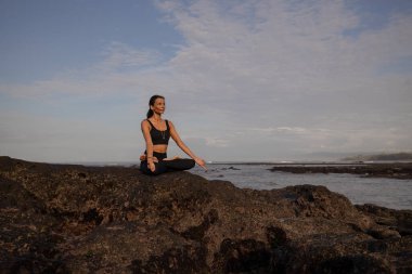 Kumsalda sabah meditasyon yogası. Lotus pozunda kayanın üzerinde oturan Asyalı kadın. Padmasana. Eller Gyan Mudra 'da. Yoga inzivası. Sağlıklı bir kavram. Uzayı kopyala Mengening Plajı, Bali, Endonezya