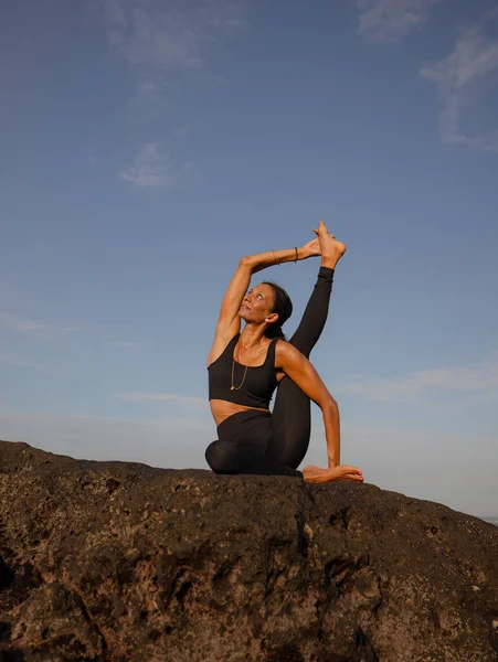 Morning outdoor yoga practice near the ocean. Asian woman practicing Eka Pada Sirsasana, Foot-behind-the-Head Pose. Flexible healthy body. Copy space. Yoga retreat. Mengening beach, Bali, Indonesia