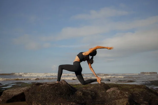 Sabah plaj yogası. Anjaneyasana 'ya alıştırma yapan Asyalı kadın. Düşük hamlede. Hilal Ay Pozu. Binicilik Pozu. Asana 'yı bükerek geri hamle yapmak. Esnek, sağlıklı, ince bir vücut. Yoga inzivası. Mengening Plajı, Bali