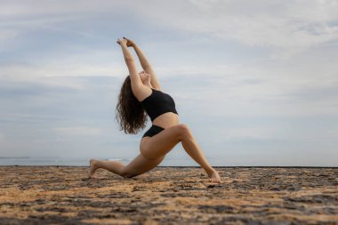 Sabahları esneme egzersizi. Sportif ve atletik genç bayan sahilde ısınıyor. Fitness, spor, sağlık konsepti. Sağlıklı bir yaşam tarzı. Aktif kadın egzersizleri. Uzayı kopyala Bali, Endonezya