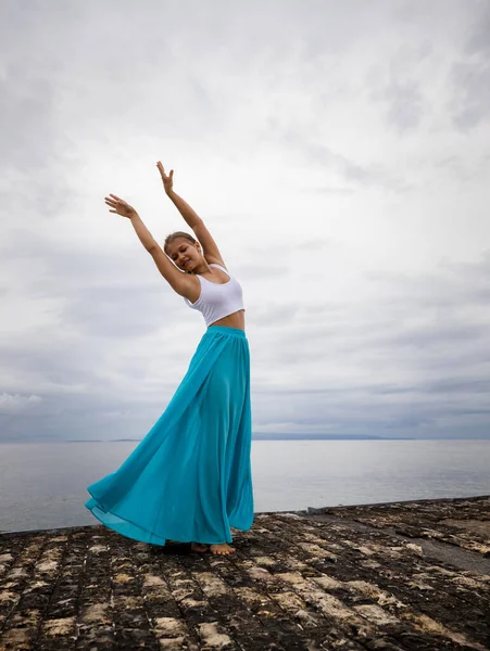 バレエのポーズを練習する美しい女性 長い青いスカートとダンスを身に着けている若いバレリーナ 屋外バレエ練習 スリムな体だ 曇った空の背景 コピースペース インドネシアのバリ — ストック写真
