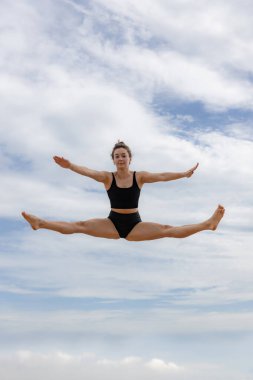 Aktif, enerjik, neşeli bir kadın bulutlu mavi gökyüzünden atlıyor. Beyaz kadın siyah spor giysisi giyiyor. Fitness, sağlık konsepti. Açık hava aktivitesi. Uzayı kopyala Gökyüzü arka planı. Bali, Endonezya