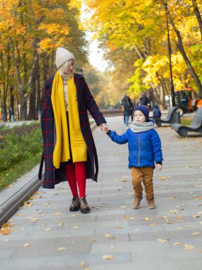 Güzel anne oğluyla birlikte sonbahar parkında yürüyor.
