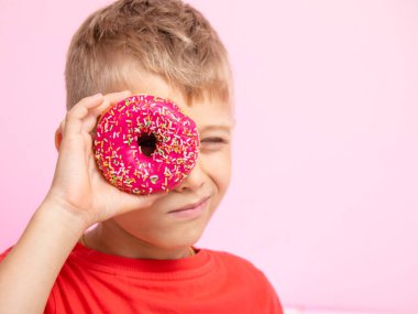 Ergen, donutları karıştırarak eğleniyordu. Bir çocuk pembe arka planda çöreklerle eğleniyor. Yiyeceklerle eğlenceli zaman