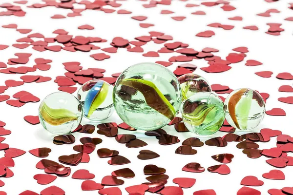 Toy marbles on white background, surrounded by so many red hearts. — Stock Photo, Image