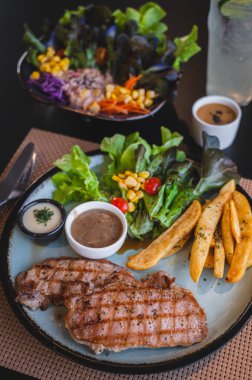 Izgara domuz eti ve patates kızartması ve salata ile biber sosu..