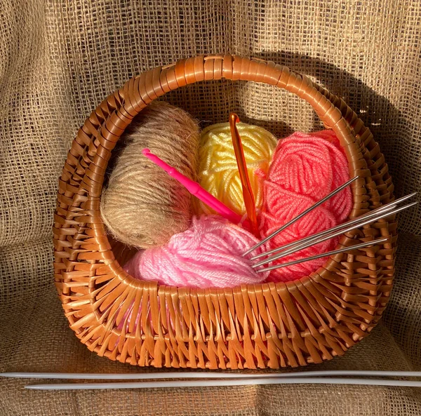 Needles in thread for knitting in a basket. Woolen threads for needlework. Basket with threads and knitting needles on a brown background.