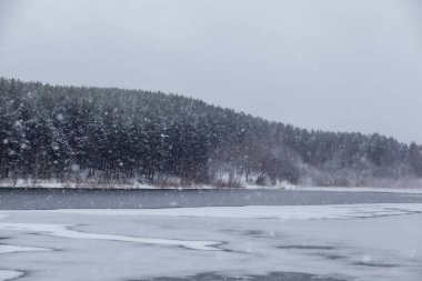 Kışın donmuş bir göl ya da nehir. Ormanın yakınında ve karlı dağlarda. Güzel kış manzaraları. Doğada kış gezileri.
