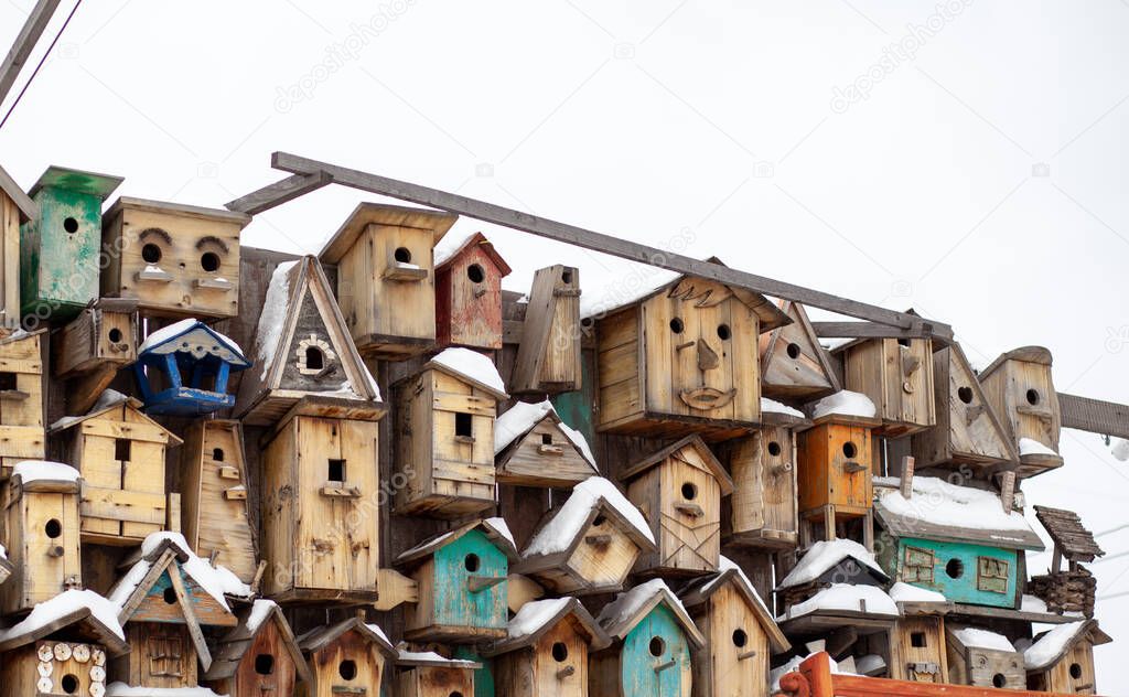 Many different forms of bird feeders. Birdhouses hang on a wooden fence. Bird feeders in the park. Beautiful designer birdhouses for feeding birds. A lot of nesting boxes or houses for feeding birds.