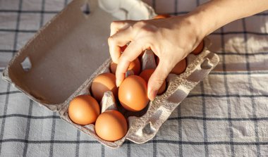 Tavuk kahverengi yumurtalar bir marketten alınan karton bir kutuda. Sağlıklı kahvaltı. Hassas yumurtaları taşımak ve depolamak için bir tepsi. Kadın paketten bir yumurtayı eliyle çıkarıyor.
