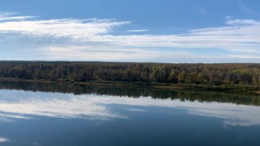 Ağaçların renkli yaprakları ve büyük beyaz bulutlar güzel bir sonbahar gününde bir göletin ya da nehrin sakin sularına yansıyor. Dinlenmek için sessiz ve güzel bir yer..