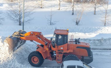Büyük turuncu traktör yoldan kar temizler ve kamyona yükler. Kışın kardan şehrin yollarının temizlenmesi ve temizlenmesi