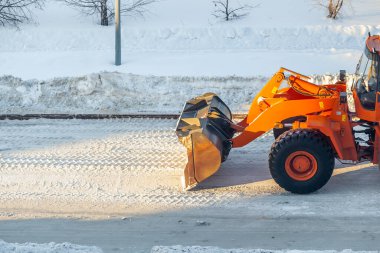 Büyük turuncu traktör yoldan kar temizler ve kamyona yükler. Kışın kardan şehrin yollarının temizlenmesi ve temizlenmesi