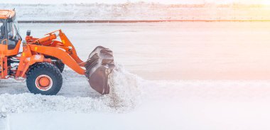 Büyük turuncu traktör yoldan kar temizler ve kamyona yükler. Kışın güneş ışığında kardan yolların temizlenmesi ve temizlenmesi.
