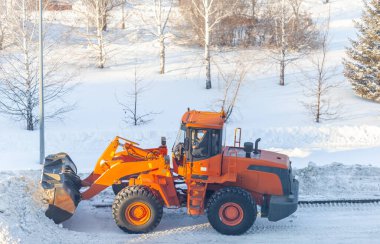 Büyük turuncu traktör yoldan kar temizler ve kamyona yükler. Kışın kardan şehrin yollarının temizlenmesi ve temizlenmesi