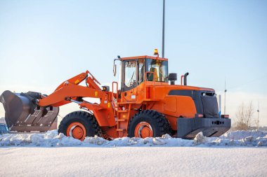 Büyük turuncu traktör yoldan kar temizler ve kamyona yükler. Kışın kardan şehrin yollarının temizlenmesi ve temizlenmesi