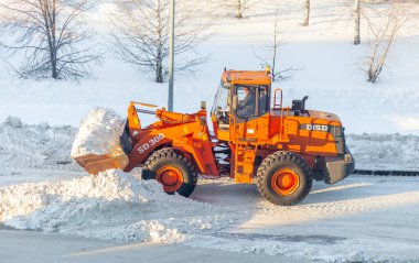 23 Aralık 2021. Kemerovo Bölgesi, Rusya. Büyük turuncu traktör yoldan kar temizler ve kamyona yükler. Kışın kardan şehrin yollarının temizlenmesi ve temizlenmesi. 