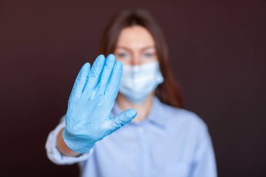 Coronavirus konsepti. Hastalıktan korunmak için maske takan ve Corona virüsünü durdurmak için el hareketi yapan bir kız. Evde kalmak için küresel çağrı. Aşıyla salgını durdurun.