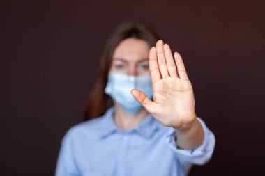 Coronavirus konsepti. Hastalıktan korunmak için maske takan ve Corona virüsünü durdurmak için el hareketi yapan bir kız. Evde kalmak için küresel çağrı. Aşıyla salgını durdurun.